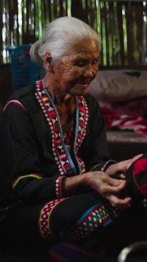 Geleneksel Asyalı kadınlar el yapımı tekstil işlerinde çalışıyorlar, ağaç bir evde dikiş dikiyorlar ve sohbet paylaşıyorlar, FullHD Dikey