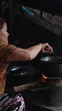 Taylandlı kadın dumanı tüten bir kömür ocağının üzerinde geleneksel ev yapımı yemekleri dikkatlice pişiriyor.