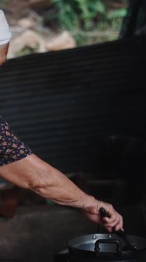 Yaşlı büyükanne geleneksel yemek pişirme yöntemlerini kullanarak köy mutfağında ev yapımı yemek hazırlıyor.