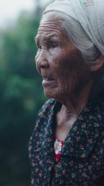 Yaşlı Asyalı kadın ahşap verandada dikey FullHD dikey kırsal alanla çevrili hayatı düşünerek duruyor.