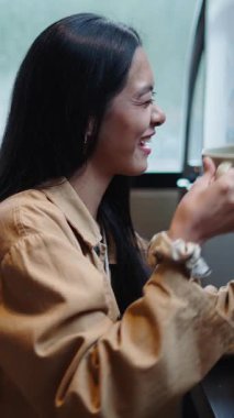 Asyalı bir kadın, FullHD dikey bir arkadaşıyla görüntülü konuşma yaparken bardaktan su içer ve yer.