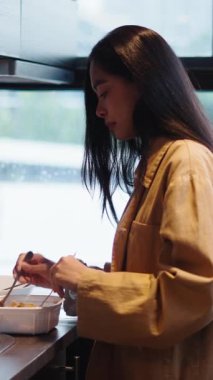 Pencere kenarında duran genç bir kadın ev yapımı yemekleri hazırlarken bir kâsede malzemeleri karıştırıyor.