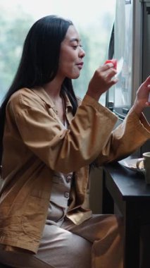 Genç Asyalı kadın, karpuz yerken video çekiyor ve akıllı telefonuyla arkadaşına yemek gösteriyor.