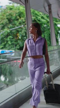 Genç trans iş kadını modern bir yürüyüş yolunda yürürken bavulunu sürüklüyor - FullHD Dikey