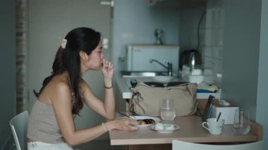 Sabah yemeğinden hoşlanan kadın, çağdaş mutfak alanı içindeki tablette dijital içeriği tarıyor.