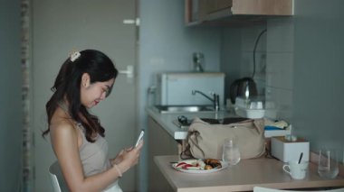 Günümüz mutfağında sabah yemeğinin tadını çıkarırken genç profesyonel akıllı telefon.