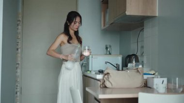 Şık mutfak tezgahının yanındaki bardağa su döken kadın.