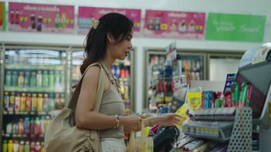 Marketteki kasada akıllı telefonla alışveriş yapan bir kadın.