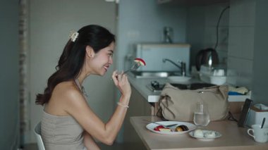 Modern ve şık mutfağında kahvaltıda meyve yiyen mutlu bir kadın.