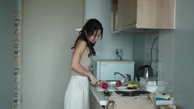 Genç bir kadın, mutfak alanında ahşap tezgahın yanında taze elma kesiyor.