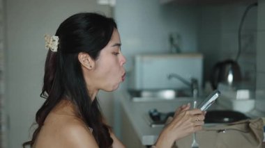 Mutfak tezgahının yanında mesajları kontrol eden bir kadın.