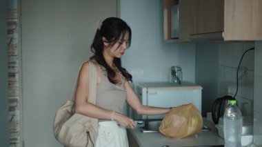 Kadın market poşetlerini boşaltıyor, mutfak tezgahının yanında taze ürünler düzenliyor.