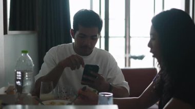 Genç çift akıllı telefonu kontrol ediyor. Sabah yemeğini paylaşırken - 4K Yatay