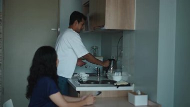 Kadın akıllı telefon kullanırken adam mutfağa sıcak su döker - 4K Yatay