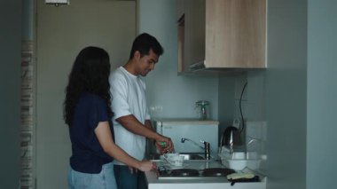 Genç çift gülüyor, birlikte bulaşıkları yıkıyor, evcil anın tadını çıkarıyor - 4K Yatay