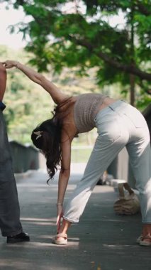 Dışarıda esneme hareketleri yapan bir kadın, yeşil manzaranın yanında spor yapan bir arkadaş.