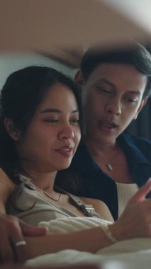 Genç çift yatakta uzanıyor, akıllı telefon ekranını paylaşıyor, sosyal medya içeriğini kaydırıyor