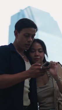 Genç çift akıllı telefon ekranını paylaşıyor, gündüz vakti birlikte şehir caddesinde yürürken samimi bir şekilde bağlanıyorlar.