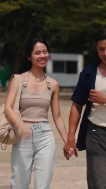 Genç Asyalı çift el ele tutuşup parkta yürüyor, romantik bir gezinti yapıyorlar.