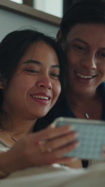 Gülümseyen çift yan yana uzanır, akıllı telefon ekranına bakar ve samimi bir anı paylaşır.