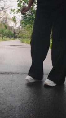 Kadın parkta siyah pantolon ve beyaz spor ayakkabı giyerek dans ediyor - 4K Yatay