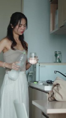 Kadın taze su dolduruyor, şık mutfak tezgahının yanında duruyor, su içiyor.