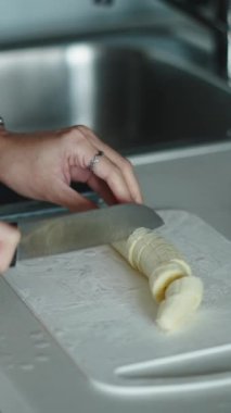 Kadın dilimlenmiş kırmızı elma tabağının yanında bir muz dilimliyor.