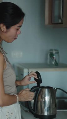 Sabah yemeği hazırlayan bir kadın. Parlak mutfak tezgahının yanındaki elektrikli su ısıtıcısına su döküyor.