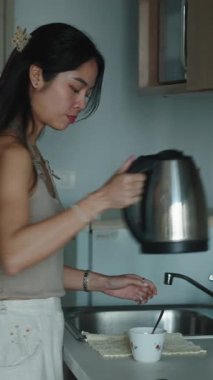 Kadın mutfağında kahvaltı hazırlıyor, bardağa sıcak su döküyor.