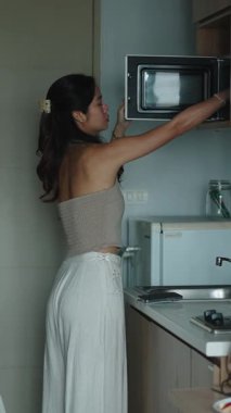 Genç bir kadın, modern ve şık bir mutfakta ısıtır, hazırlar ve sağlıklı bir kahvaltı yapar.