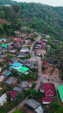 Canlı yeşil bir dağ manzarasının ortasına kurulmuş sakin bir köyün yüksek açılı görüntüsü.