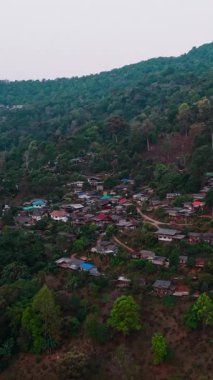 Tayland 'ın yemyeşil manzarasında, dik yamaçlarda kümelenmiş canlı evler, geleneksel kırsal yerleşim yerlerini ortaya koyuyor.