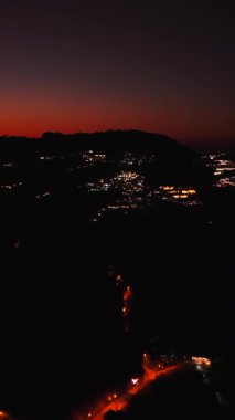 Parlayan şehir ışıkları alacakaranlıkta dağlık araziyi aydınlatıyor.