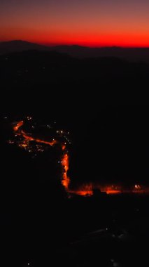 Parlak sokak lambaları altın günbatımında dönen dağ yolunu aydınlatıyor.