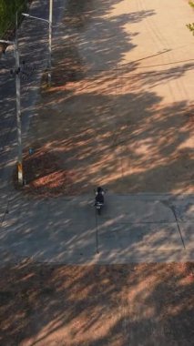Person riding a scooter on a dirt road next to a paved street during a sunny afternoon