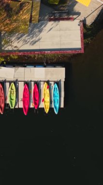 Top down aerial view of colorful kayaks and a pedal boat moored at a floating dock on a calm lake