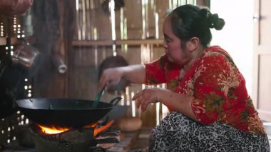 Traditional cooking scene capturing a skilled Asian woman preparing fresh tea leaves over a wood fire in a rustic and authentic kitchen environment - 4K Horizontal