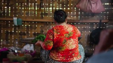 Traditional lahu woman extracting the boiled tea leaves from the fire and placing them on a wicker tray for drying - 4K Horizontal