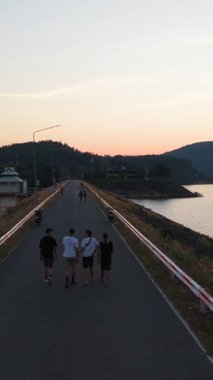 Group of tourists walking on a dam road during a beautiful sunset - FullHD Vertical