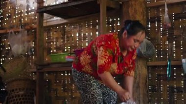 Southeast Asian woman carefully preparing a home-cooked meal inside a traditional rural kitchen with rustic bamboo walls - 4K Horizontal