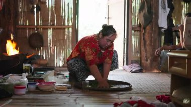Experienced Asian woman barefoot draining boiled tea leaves on a wicker tray near the fire - 4K Horizontal