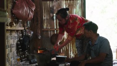 Southeast Asian couple preparing a meal together on a wood stove in their simple kitchen - 4K Horizontal