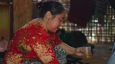 Woman dressed in traditional lahu clothes in a simple rural house carefully pouring and calmly drinking herbal tea - 4K Horizontal