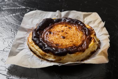 Parşömen kağıdında İspanyol Bask peynirli keki, siyah tahta üzerinde, yakın çekim