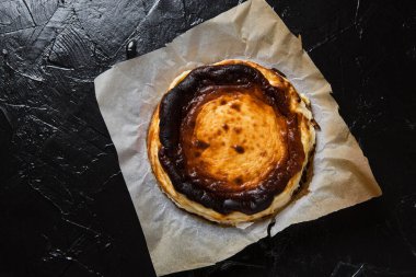 Yeni pişmiş Bask peynirli keki parşömen kağıdında, siyah tahtada, düz yerde.