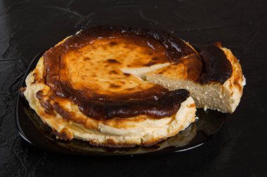 Siyah bir tabakta İspanyol cheesecake 'i, siyah bir levhada, tüm tatlıdan bir parça kesilir, yakın plan.