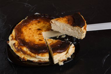 Siyah bir tabakta İspanyol Bask peynirli keki, siyah bir levha üzerinde, iki parça kesilmiş ve biri bir bıçakla, konsept üzerinde büyütülmüş.