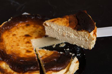 Bir parça Bask peynirli keki, tatlı parçalarının üzerinde bir bıçakla büyütülür, seçici odaklanma, yakın plan.