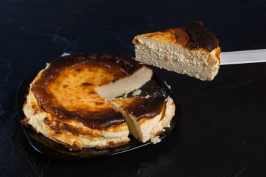 Siyah bir tabakta, siyah bir levhada Bask peynirli keki, iki parça kesilmiş ve biri bıçağın üstünde duruyor, konsept olarak.