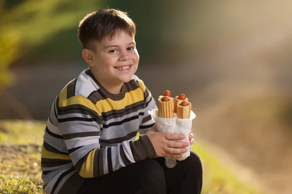 A boy in a striped sweater, with four hot dogs in his hands, laughs merrily, breakfast in nature